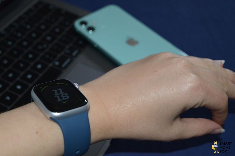 Apple Watch Series 9 am Handgelenk vor Macbook und iPhone